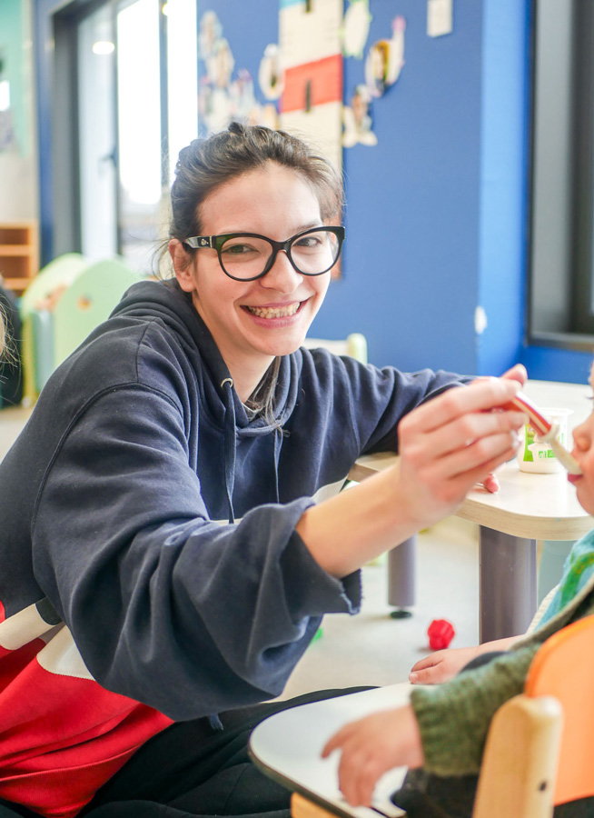 femme souriante en train de donner à manger à un bébé - Équipe pédagogique de la crèche multilingue